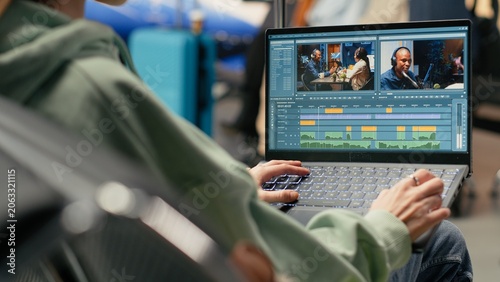 Billede på lærred Digital nomad filmmaker cutting video clips and applying color grading on laptop in the airport terminal, preparing web content during travel, remote creative work and global mobility on a trip