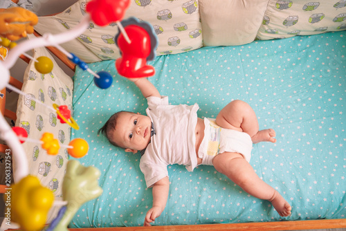 The baby's tiny hands reach toward the hanging toys as they lie peacefully on the blue blanket in the crib.