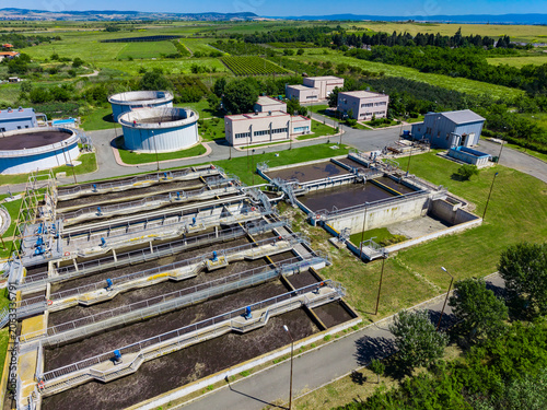 Wastewater treatment facility in rural area with large tanks and buildings under clear blue sky during daytime