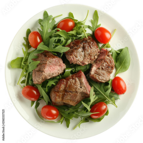 Down view of grilled beef steak medallions arranged on a bed of fresh green arugula with bright red cherry tomatoes on a white plate