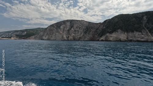Drone aerial footage of dramatic rocky cliffs rising above the crystal-clear waters of the Ionian Sea near Lefkada, Greece. Scenic Mediterranean coastline with rugged terrain, blue water 