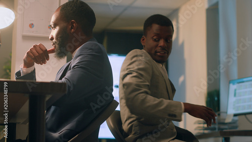 Φωτογραφία Friendly businessman having fun at work during nightshift, bumping into colleague using desk chair, coworkers racing eachother to get out of tedious routine during overnight stay in office