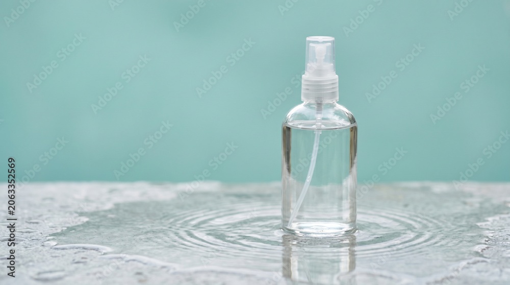 Obraz premium Clear spray bottle with liquid on a wet surface and blue background