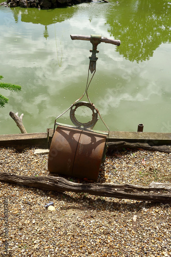 A rusty old garden roller next to a small pond