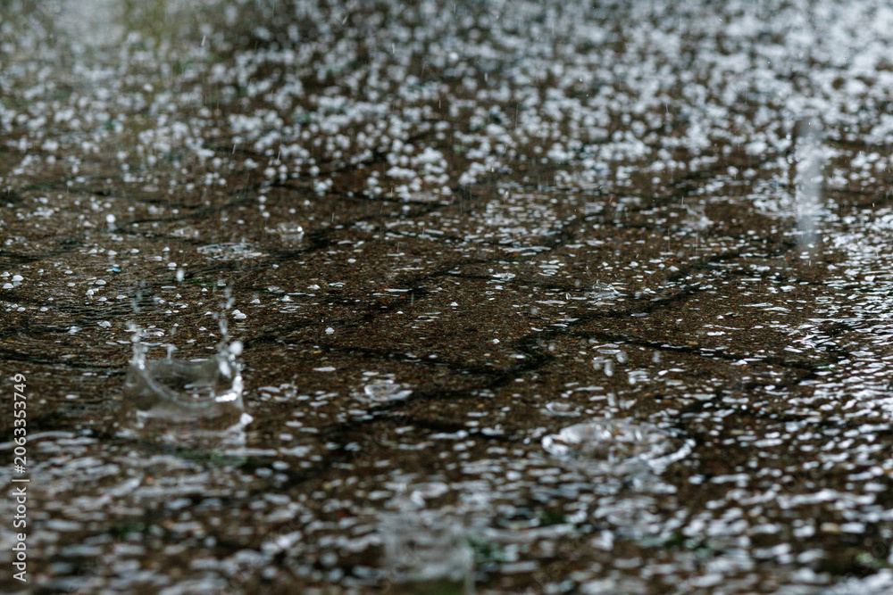 Fototapeta premium hailstones falling during severe summer storm with splashing raindrops on wet pavement