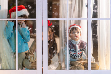 Excited children in Santa hats open Christmas presents together by a decorated tree and cozy fireplace at home.