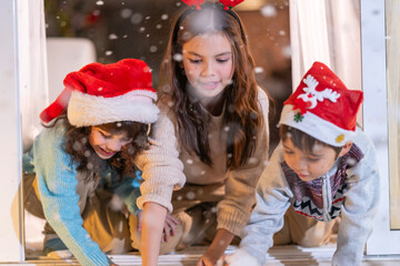 Excited children in Santa hats open Christmas presents together by a decorated tree and cozy fireplace at home.