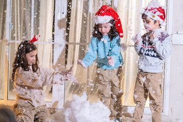 Children in Santa hats and reindeer antlers gather by a glowing decorated Christmas tree opening gifts at home.