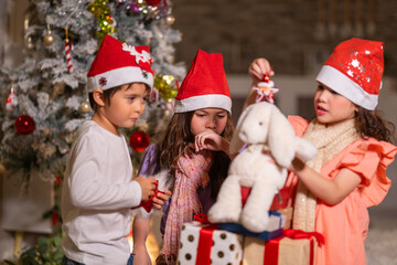 Smiling girl hugs a soft teddy bear gift beside the Christmas tree during a joyful family holiday celebration.