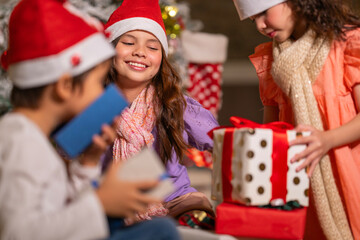 Smiling girl hugs a soft teddy bear gift beside the Christmas tree during a joyful family holiday celebration.