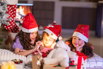 Happy children play with soft fake snow by a window during a festive Christmas morning celebration indoors at home together.