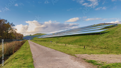 Wijster, Netherlands - 27 October 2024: View of the solar farm on the former VAM landfill hill with solar panels installed on grassy slopes under a blue sky with white clouds.