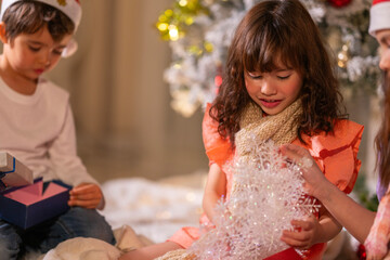 Smiling girl hugs a soft teddy bear gift beside the Christmas tree during a joyful family holiday celebration.