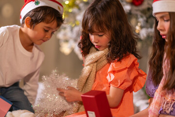 Smiling girl hugs a soft teddy bear gift beside the Christmas tree during a joyful family holiday celebration.