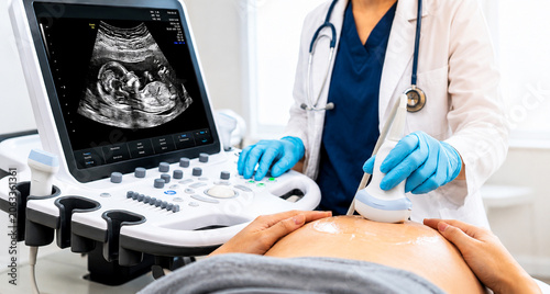 Pregnant woman receiving ultrasound scan in modern medical clinic with fetal image displayed on monitor, prenatal healthcare concept.