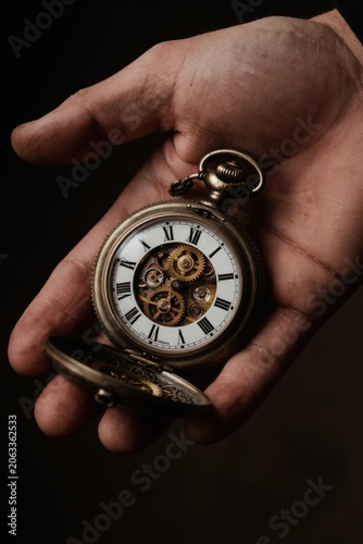 Man holds antique pocket watch revealing complex internal gears. Intricate timepiece with roman numerals. Classic accessory shows mechanical precision, fine craftsmanship. Vintage horologe signifies