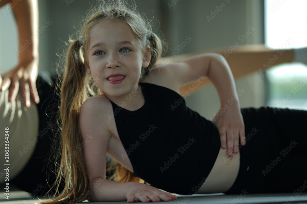 Naklejka premium Mother and young daughter stretch and exercise together on a mat in a bright gym, sharing a healthy active lifestyle.
