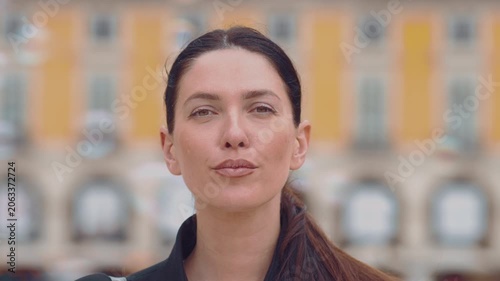 Woman stands in square in Lisbon. She closes her eyes and shows various expressions while looking straight ahead. The sun shines on her face as she interacts with the camera.