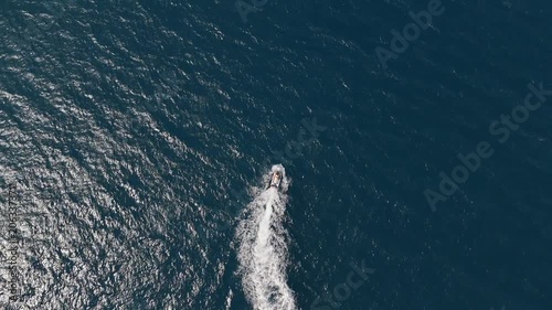 Drone top-down aerial footage of a jet ski creating a white wake across the deep blue waters of the Ionian Sea near Greece. Summer recreation, water sports and Mediterranean travel destination concept