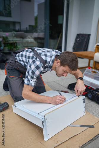 Man measures furniture panel with ruler and pencil during DIY assembly