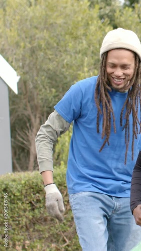 Vertical video: Laughing man in hat holding green bag as teammate dropping debris walking off park