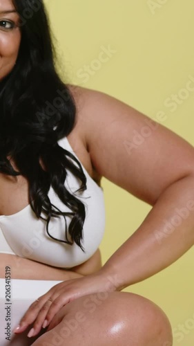Vertical video: Smiling model shifting torso on pale yellow backdrop in white bra bottoms rings
