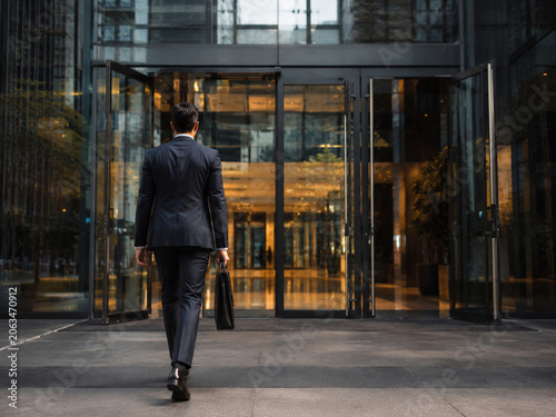 Businessman Walking with a Briefcase Towards a Modern Office Building Entrance