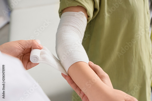 Obraz na plátně Medical professional applying white elastic bandage to childs injured arm, first