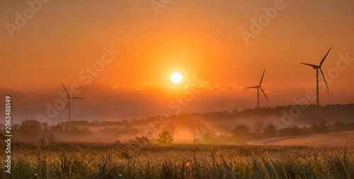 Golden Sunset Landscape with Wind Turbines Silhouette Over Green Field, Misty Countryside Scenery Representing Renewable Energy and Sustainable Future