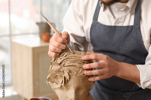 Billede på lærred Young male sculptor carving clay bust in workshop, closeup