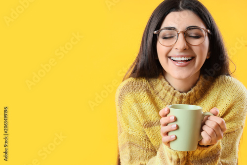 Happy young woman with cup of tea on yellow background, closeup