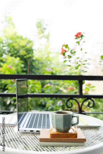 Green coffee cup and laptop and notebooks , cozy balcony outdoor