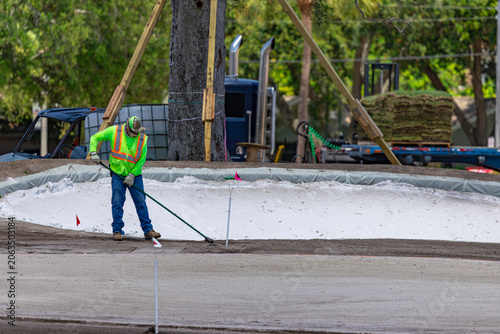 Construction worker leveling sand with rake during golf course bunker renovation project