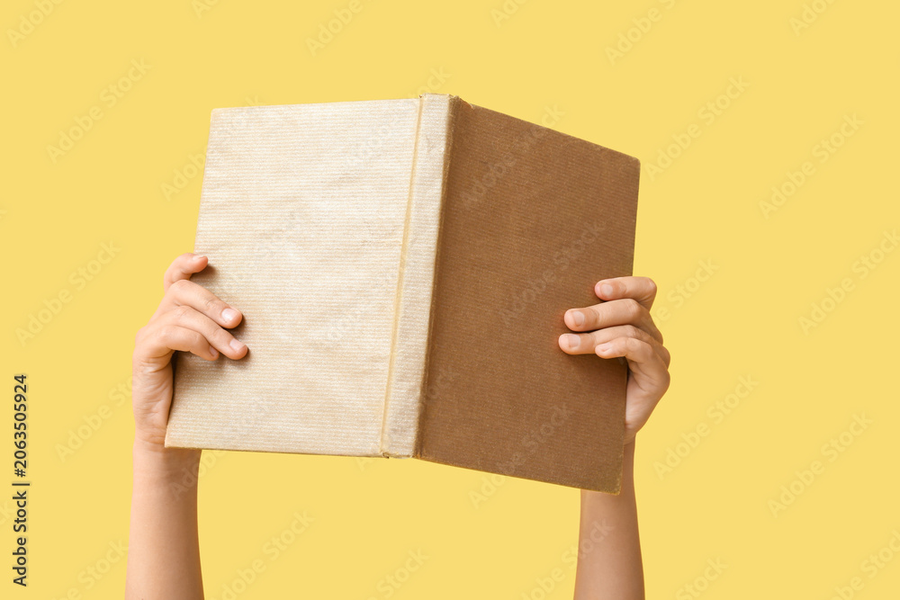 Naklejka premium Hand of little girl holding open book on yellow background