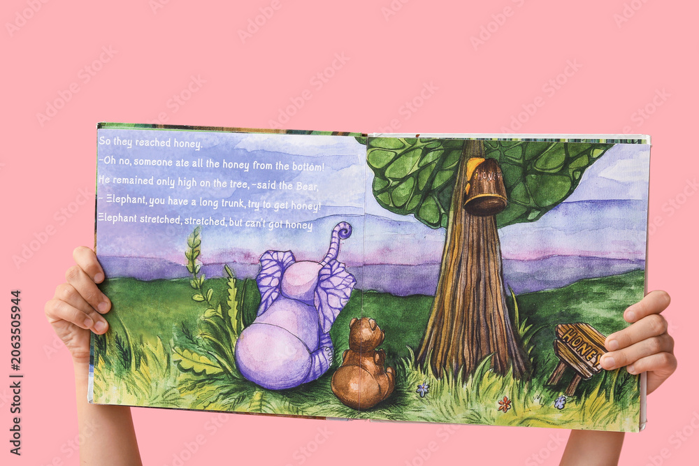 Naklejka premium Hands of little girl holding open fairy tale book on pink background