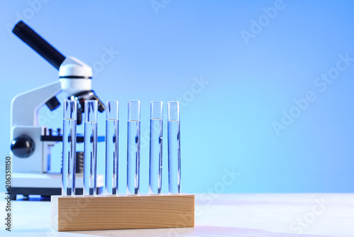 Holder with test tubes and modern microscope on white table