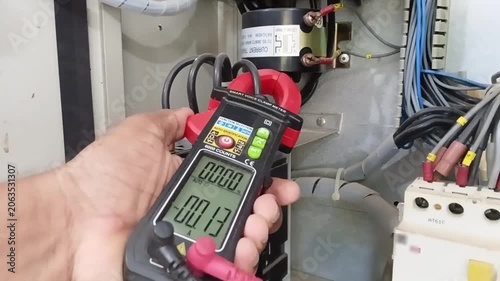 Electrician measuring low neutral current 0.16A using clamp meter to verify perfect phase balance on industrial MCCB breaker panel
