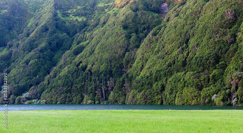 Naklejka premium Sete Cidades volcanic crater lakes. Lush green hills surround twin lagoons. Dense forest covers steep caldera walls. Scenic Azores landscape in Portugal's San Miguel Island.