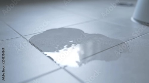 Puddle of water leaking on white bathroom tiled floor.