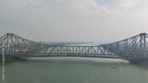 A spectacular aerial drone perspective of the historic Howrah Bridge (Rabindra Setu) spanning the Hooghly River, showcasing the iconic cantilever engineering marvel of West Bengal, India.