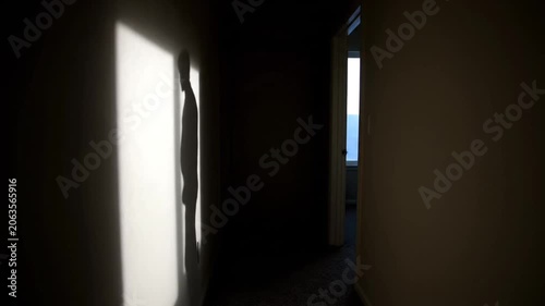 Silhouette of a man walking past a bright light in a dark hallway.