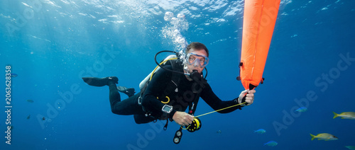 Diver holding a surface marker buoy underwater in clear blue ocean  