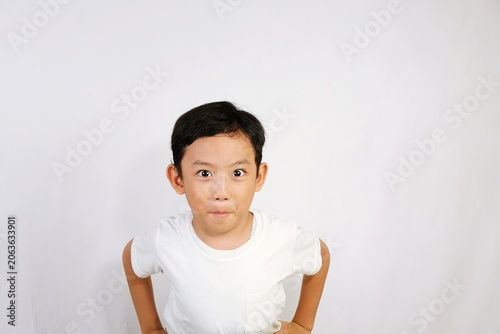 Playful little Asian boy making funny facial expression in minimalist studio with clean white background and cheerful mood.