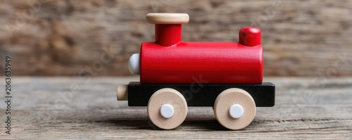 A small red and black wooden toy train sits on a wooden surface with a rustic wooden background.