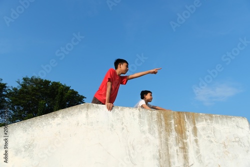 Energetic young boy pointing toward distance while playing outdoors with dramatic blue sky and urban adventure atmosphere.