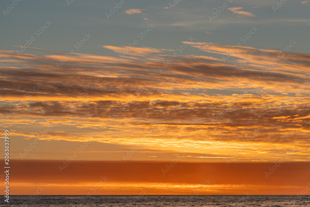 Fototapeta premium Sunset over water, vibrant hues orange, pink, yellow, scattered clouds, sky reflection on water, horizon line, vastness, tranquility, no objects or people, distant perspective, warm lighting, reali