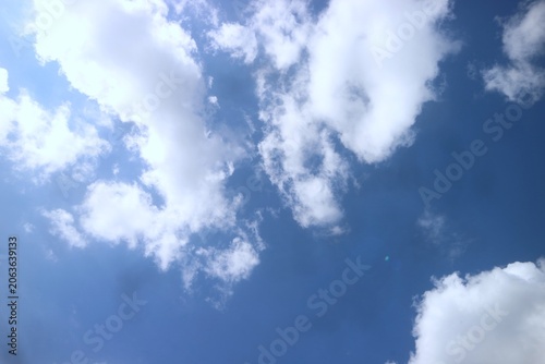 A serene and expansive blue sky filled with soft, white cumulus clouds, beautifully illuminated by the bright, warm sunlight on a clear day, evoking a deep sense of natural beauty and tranquility
