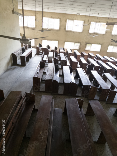 Empty university lecture hall with tiered seating and wooden desks, interior of an aging academic classroom illuminated by natural daylight through barred windows, educational infrastructure and learn