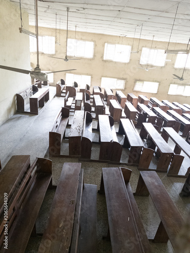 Empty university lecture hall with tiered seating and wooden desks, interior of an aging academic classroom illuminated by natural daylight through barred windows, educational infrastructure and learn