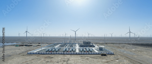 Grid-Scale Battery Storage Facility Surrounded by Wind Turbine Array in Gobi Desert Under Bright Sun